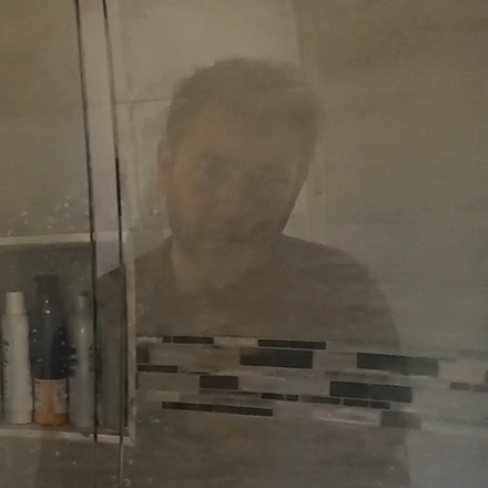Faint reflection of a man's face in shower glass, before redaction